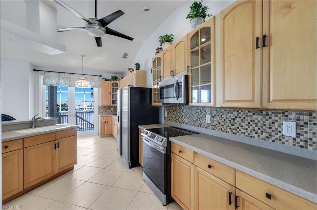 Kitchen with glass insert cabinets, light wood finish cabinetry, stainless steel appliances, backsplash, and lofted ceiling