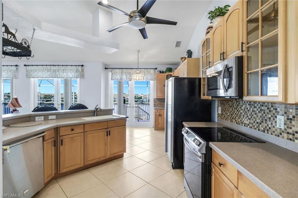 Kitchen with glass fronted cabinets, stainless steel appliances, decorative backsplash, a ceiling fan, and light countertops