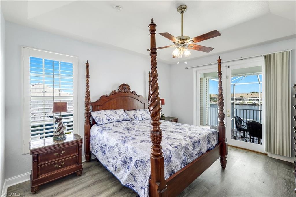Bedroom with wood finished floors, access to exterior, ceiling fan, and a water view