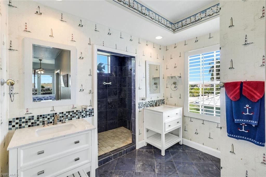Bathroom with two vanities, wallpapered walls, a stall shower, and ceiling fan