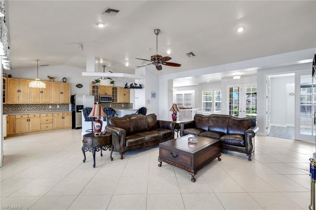 Living room with ceiling fan, french doors, vaulted ceiling, and light tile patterned floors