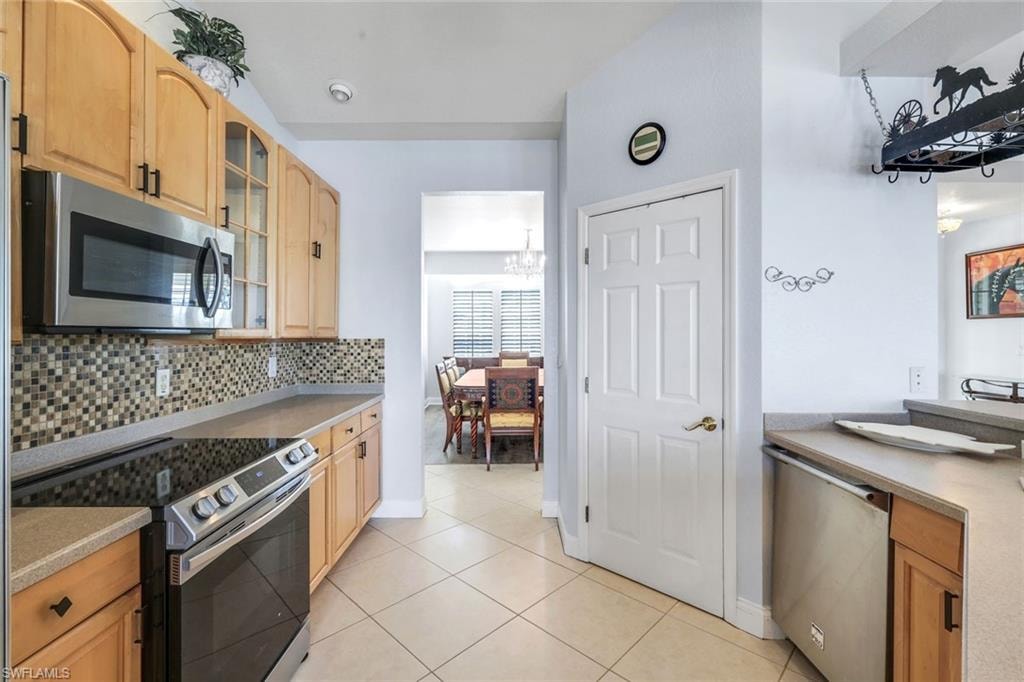 Kitchen with stainless steel appliances, glass fronted cabinets, light wood finish cabinetry, light tile patterned flooring, and hanging lights