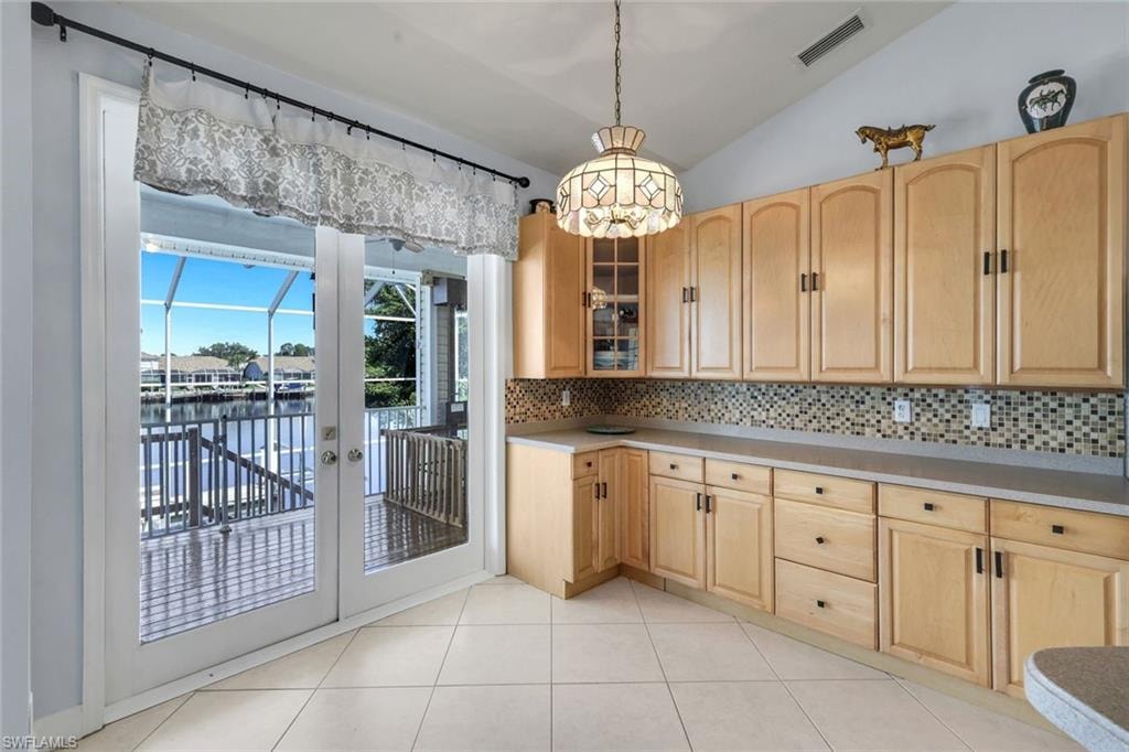 Kitchen with light wood finish cabinets, lofted ceiling, glass fronted cabinets, decorative backsplash, and light countertops