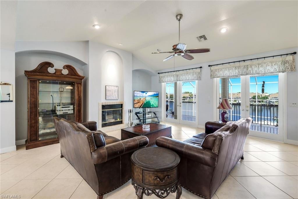 Living area with light tile patterned floors, a ceiling fan, french doors, a tiled fireplace, and lofted ceiling