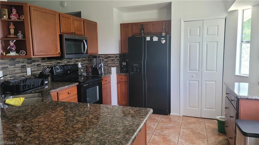 Kitchen featuring black appliances, dark stone countertops, sink, backsplash, and light tile patterned flooring