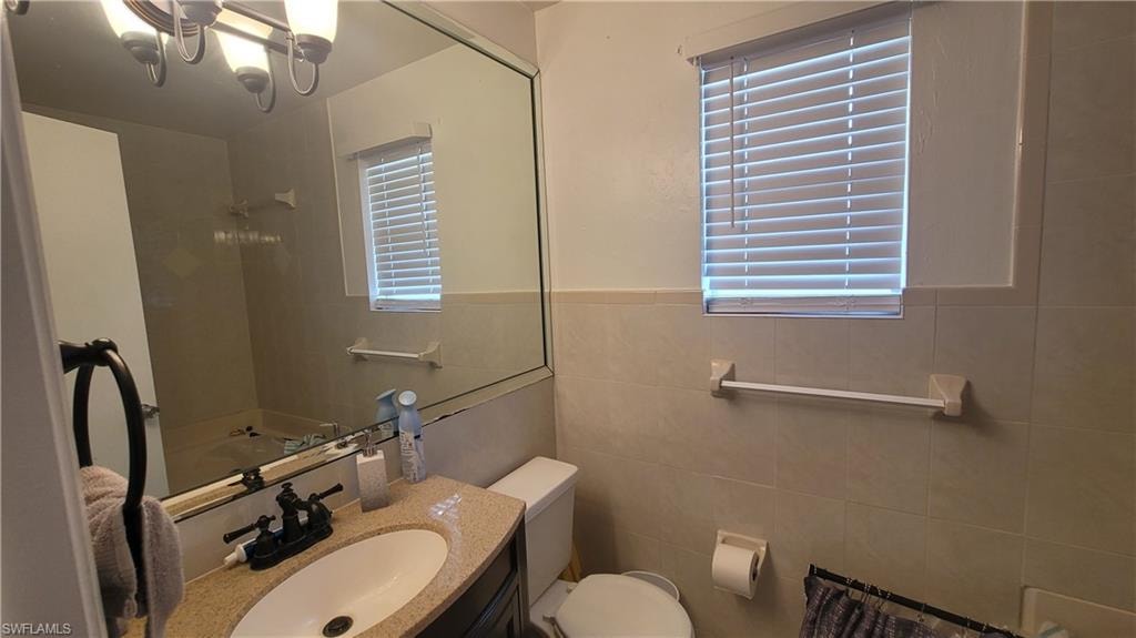 Bathroom featuring tile walls, a wealth of natural light, toilet, and vanity