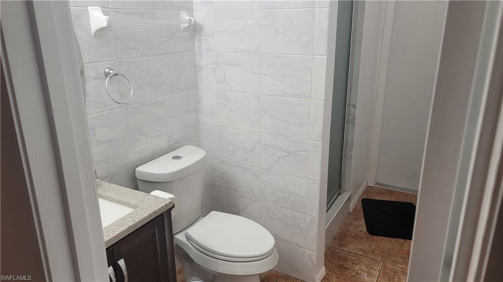 Bathroom with walk in shower, toilet, vanity, tile walls, and tile patterned floors