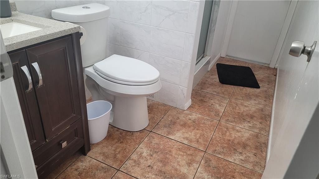 Bathroom featuring a shower with shower door, toilet, vanity, tile walls, and tile patterned floors