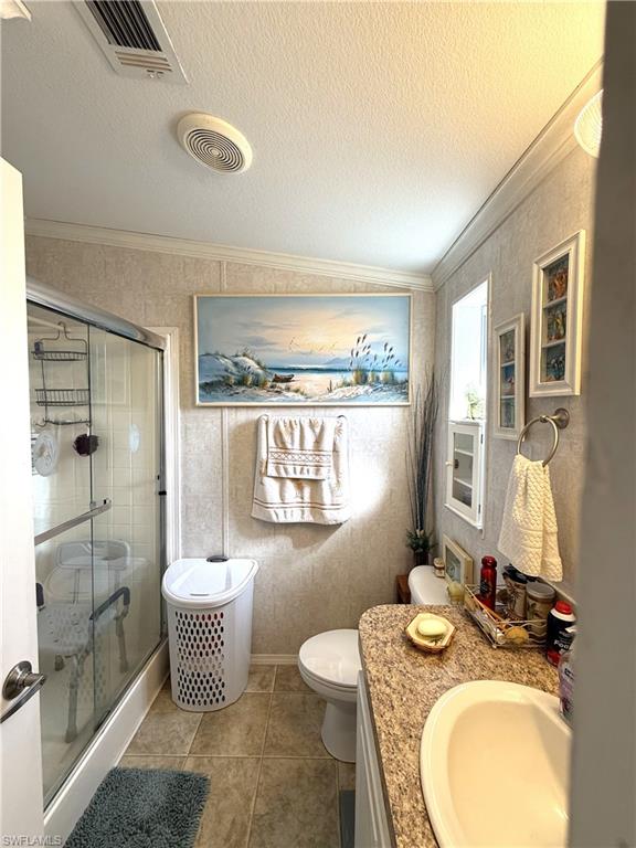 Full bathroom featuring vanity, a stall shower, a textured ceiling, light tile patterned floors, and crown molding