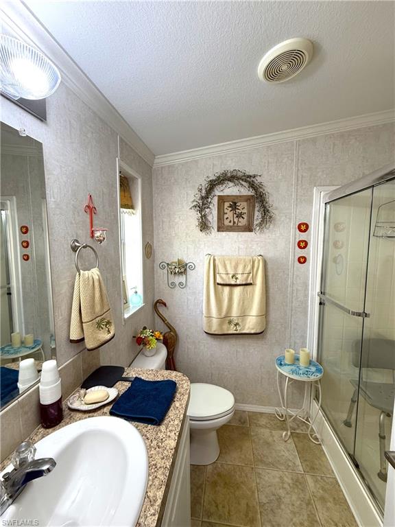 Bathroom featuring vanity, a shower stall, ornamental molding, a textured ceiling, and light tile patterned floors