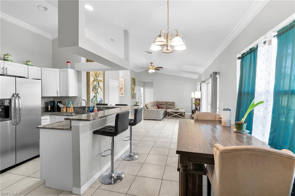 Kitchen with crown molding, stainless steel fridge with ice dispenser, dark stone counters, white cabinetry, and a chandelier