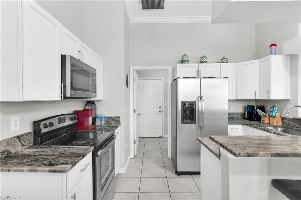 Kitchen featuring stainless steel appliances, white cabinetry, a peninsula, light tile patterned floors, and crown molding