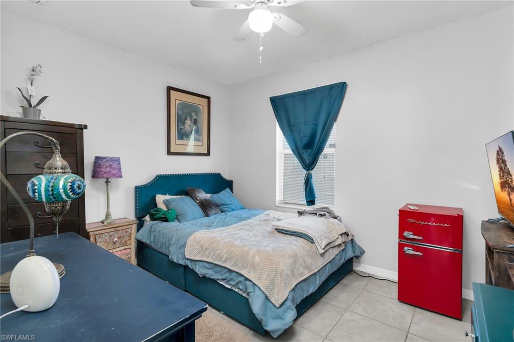 Bedroom with freestanding refrigerator, ceiling fan, and light tile patterned floors