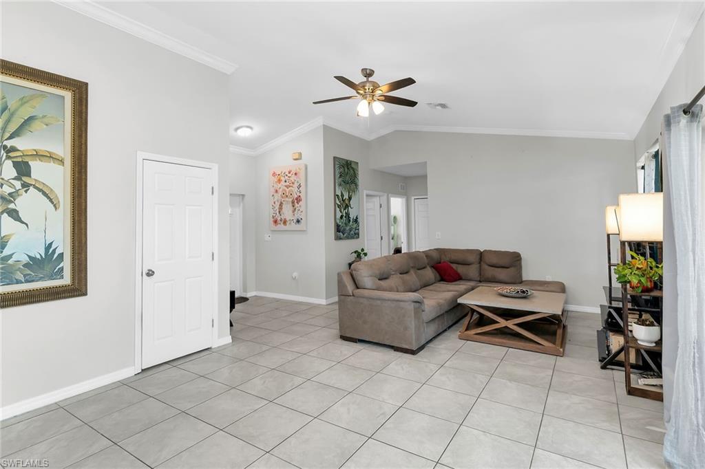 Living area with crown molding, vaulted ceiling, ceiling fan, and light tile patterned flooring