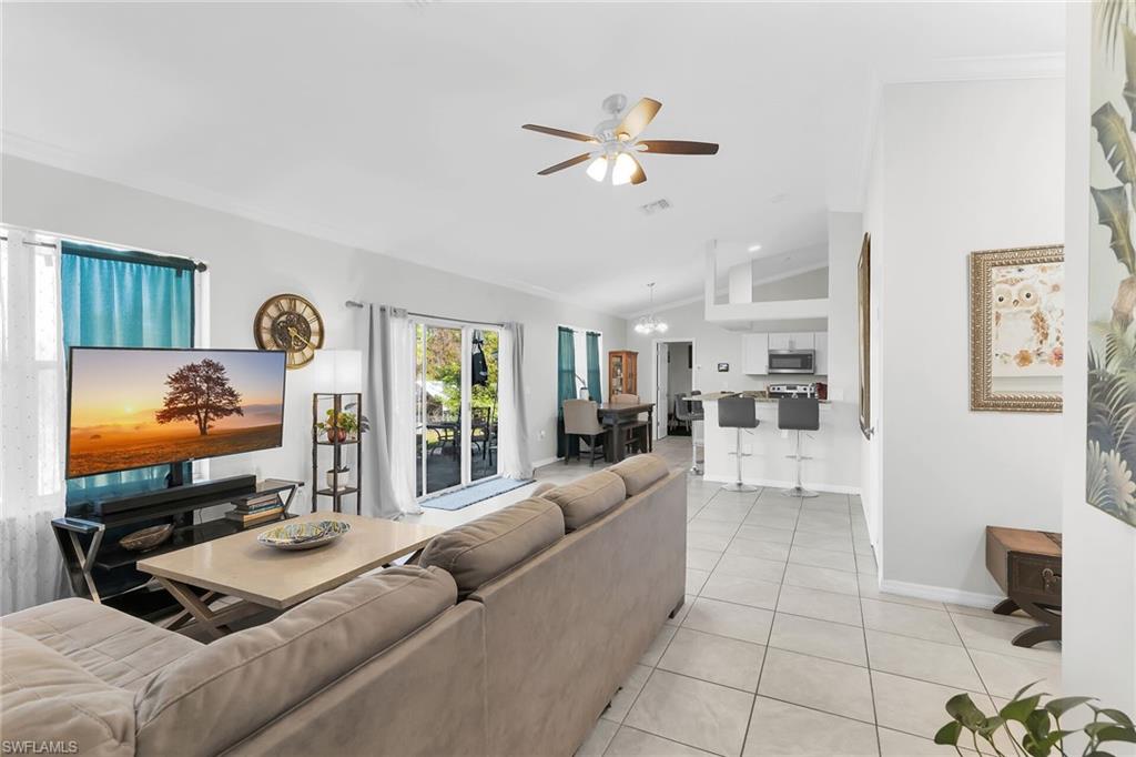 Living room with light tile patterned floors, ceiling fan, lofted ceiling, and ornamental molding