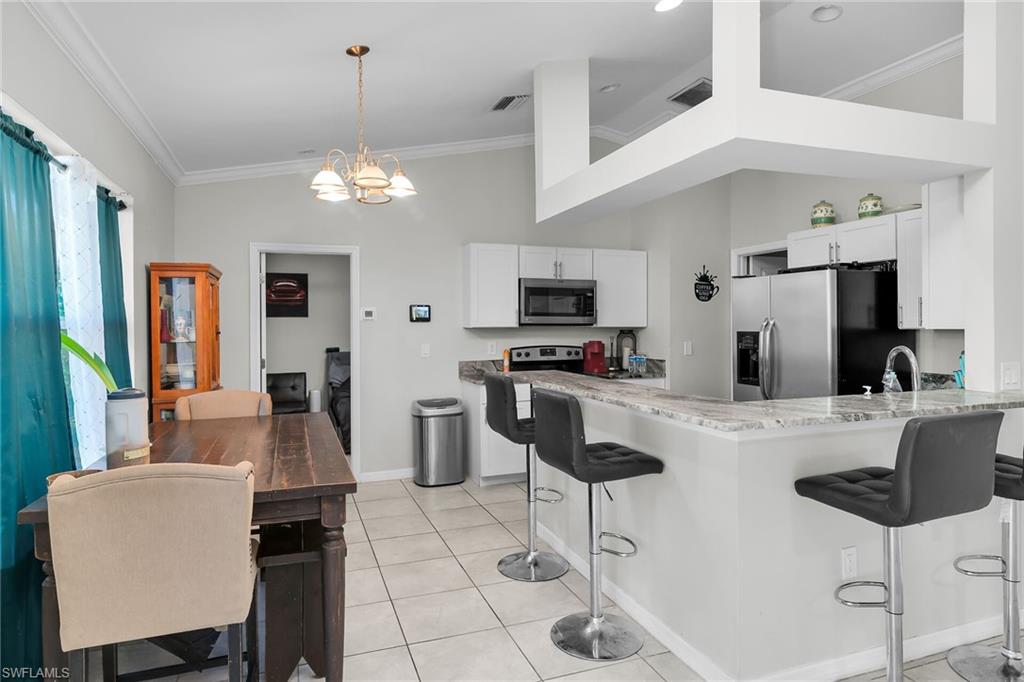 Kitchen with a breakfast bar area, light stone countertops, ornamental molding, suspended lighting, and a peninsula