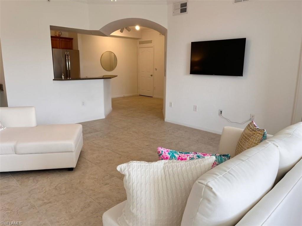 Living room featuring arched walkways, light tile patterned floors, and crown molding