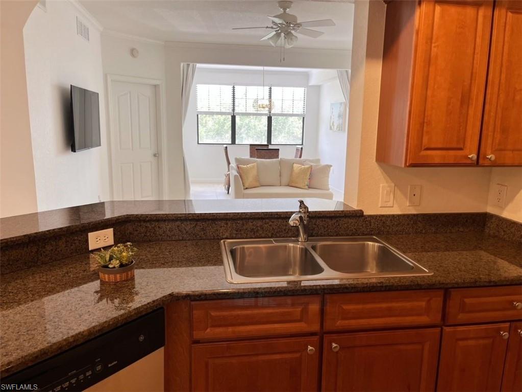 Kitchen with dishwasher, brown cabinetry, open floor plan, dark stone countertops, and a ceiling fan