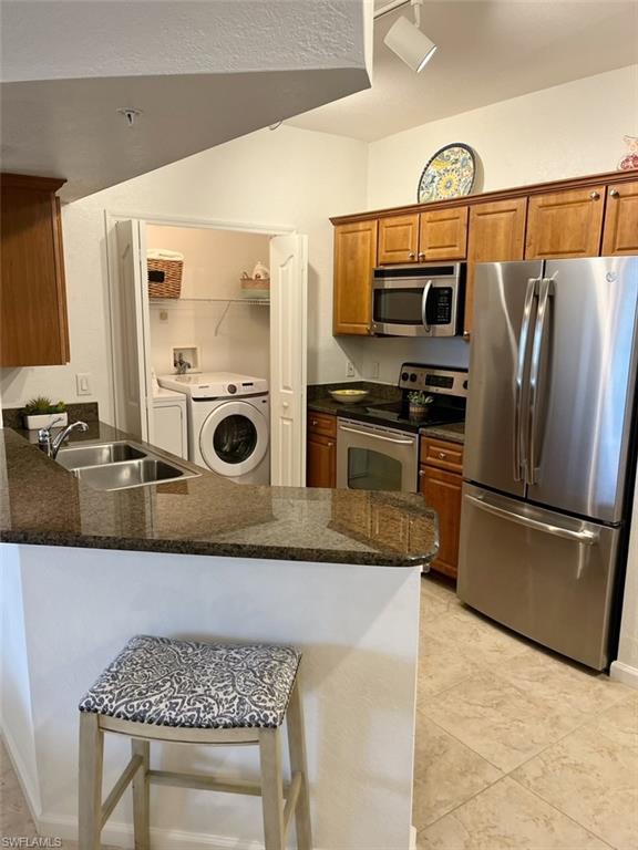 Kitchen featuring stainless steel appliances, brown cabinetry, a kitchen bar, dark stone countertops, and a peninsula