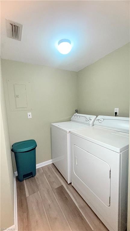 Laundry area featuring light wood-style flooring, washing machine and dryer, and electric panel