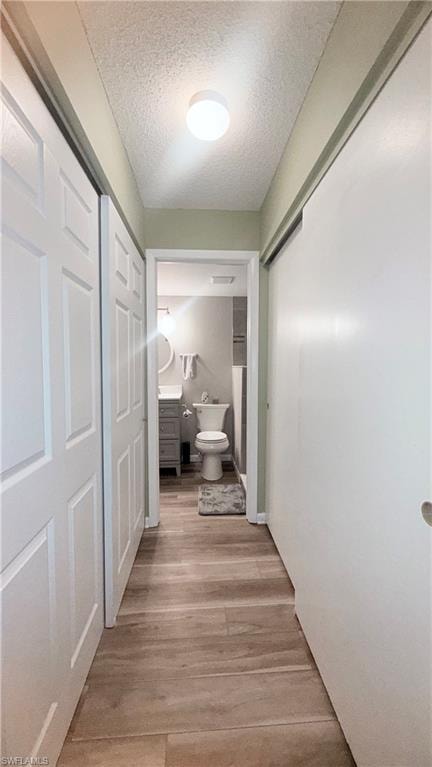 Corridor with light wood finished floors and a textured ceiling