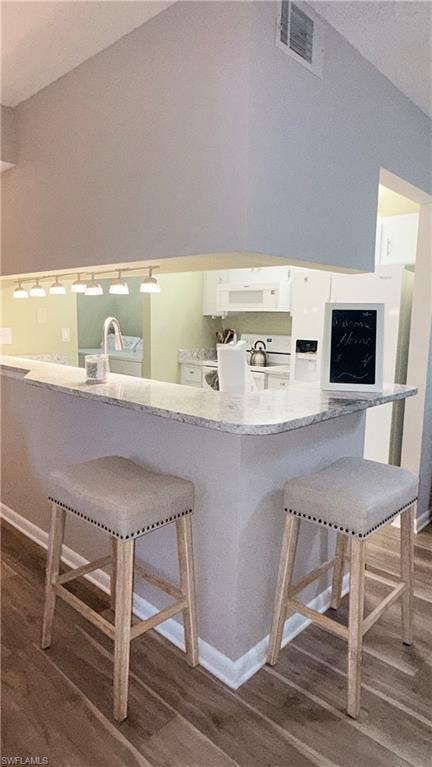 Kitchen with a kitchen bar, dark wood-type flooring, white appliances, lofted ceiling, and light stone counters