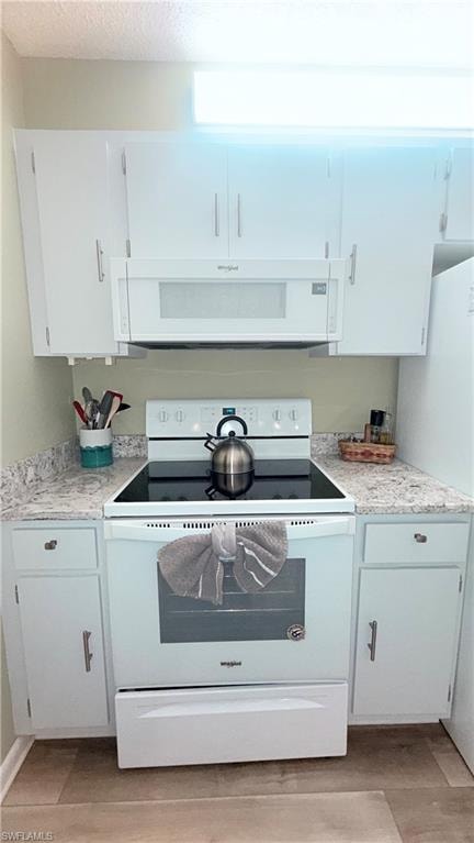 Kitchen with white appliances, light countertops, white cabinetry, light wood finished floors, and a textured ceiling