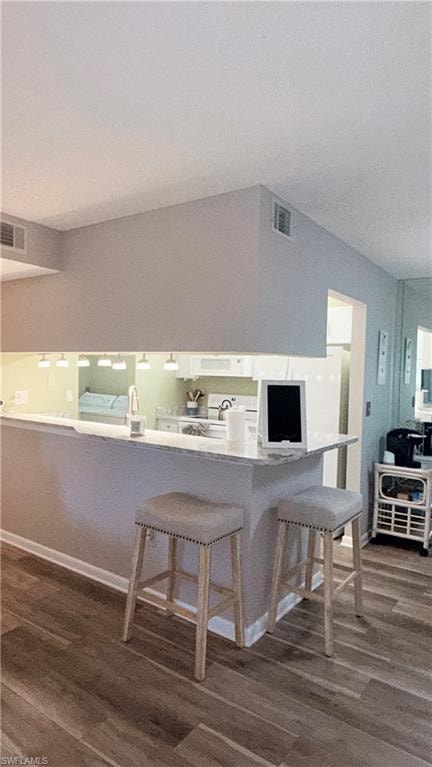 Kitchen with dark wood finished floors, a breakfast bar area, white appliances, and white cabinets