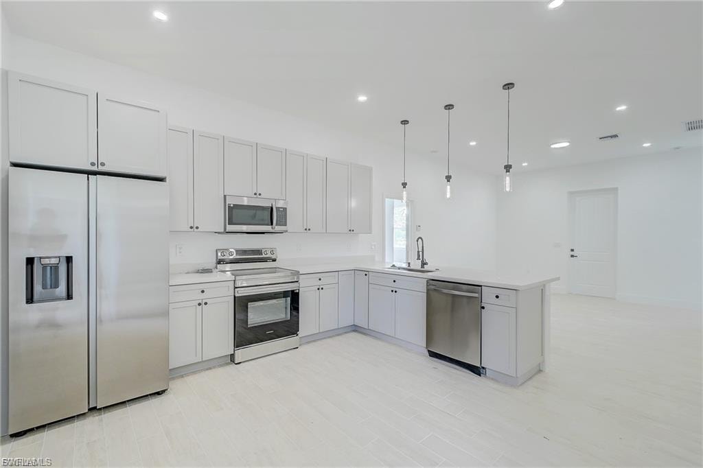 Kitchen with stainless steel appliances, hanging light fixtures, white cabinetry, and a peninsula