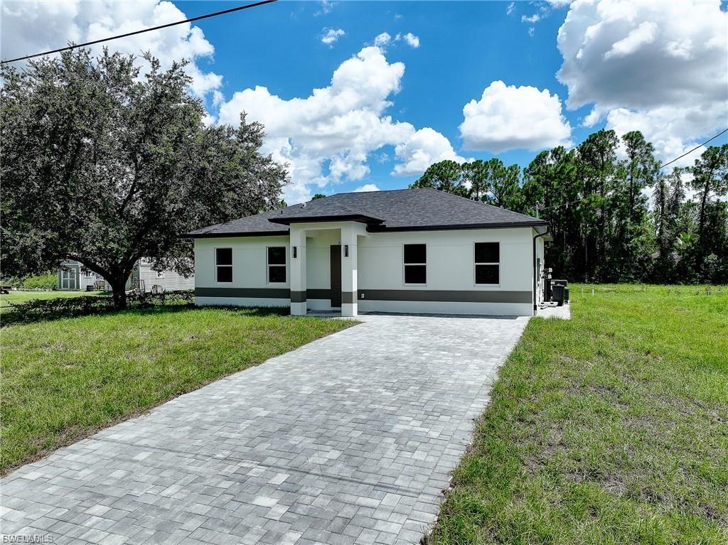 View of front facade featuring a front lawn, stucco siding, and decorative driveway
