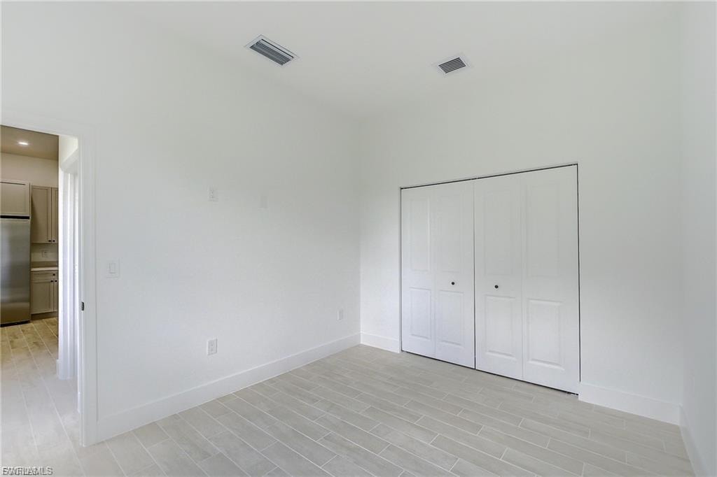Unfurnished bedroom featuring stainless steel fridge, wood tiled floors, and a closet