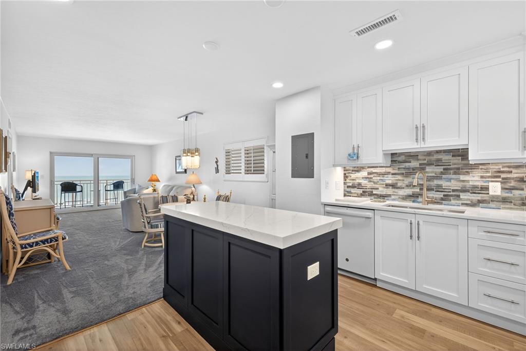 Kitchen with open floor plan, white dishwasher, light stone counters, light wood finished floors, and dual tone cabinetry