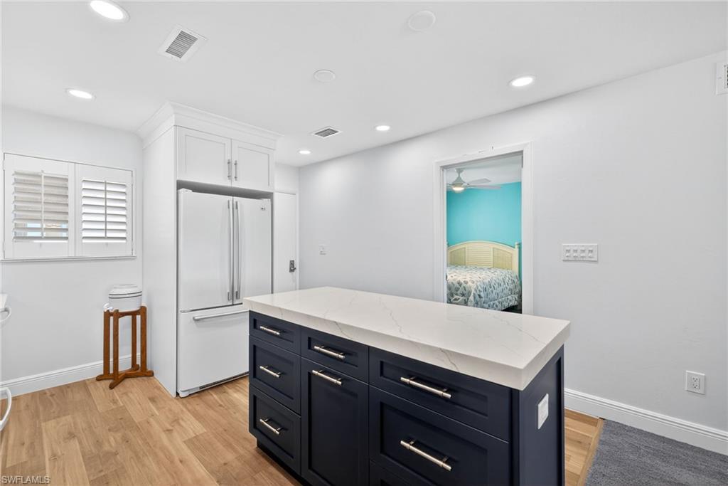 Two tone kitchen with freestanding refrigerator, light stone countertops, a kitchen island, light wood-type flooring, and two tone cabinets