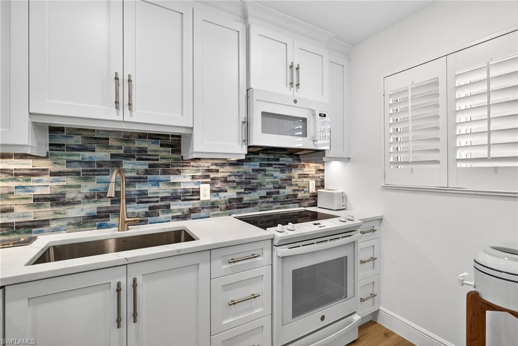 Kitchen with white appliances, white cabinets, light stone counters, light wood-type flooring, and tasteful backsplash