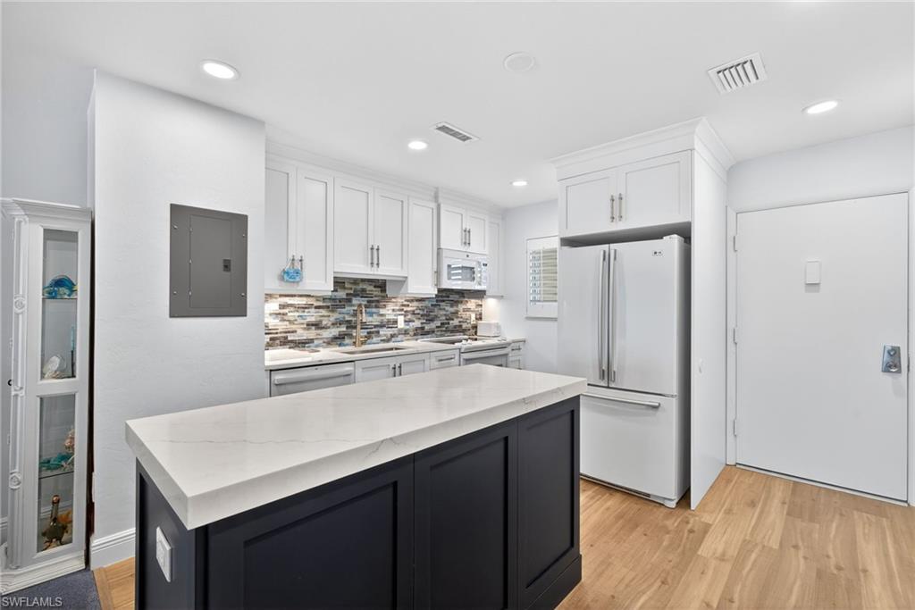 Two tone kitchen with light wood-style floors, white appliances, electric panel, backsplash, and two tone cabinetry