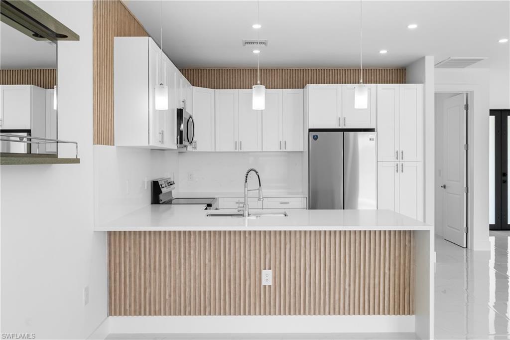 Kitchen with stainless steel appliances, white cabinetry, light stone countertops, and a peninsula