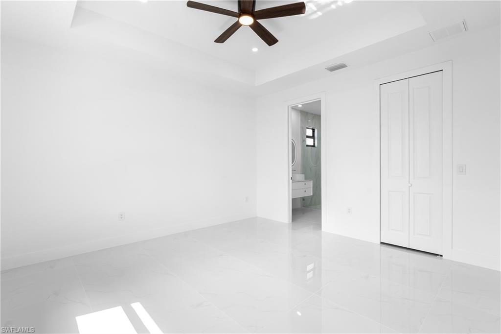 Unfurnished bedroom featuring a tray ceiling, ensuite bathroom, a ceiling fan, and recessed lighting