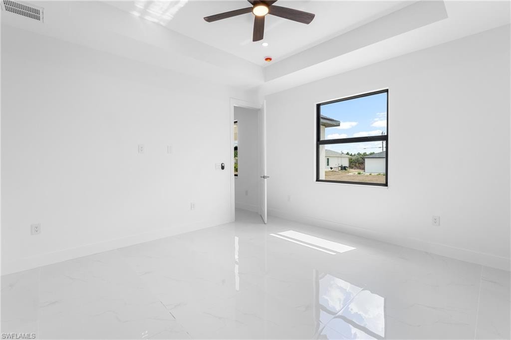 Empty room featuring a raised ceiling, light marble finish floors, ceiling fan, and recessed lighting