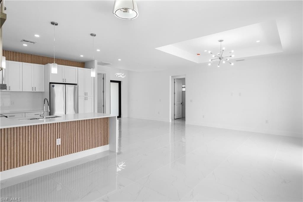 Kitchen with white cabinetry, freestanding refrigerator, a chandelier, light stone counters, and light marble finish floors