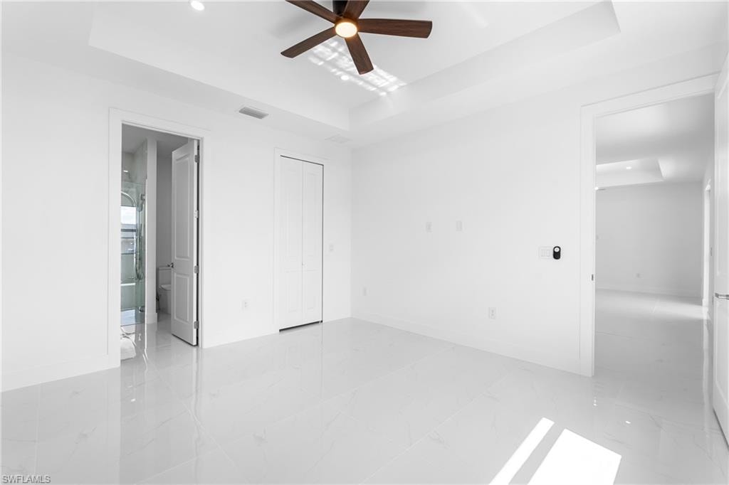 Unfurnished bedroom with a tray ceiling, ceiling fan, a closet, recessed lighting, and light marble finish floors