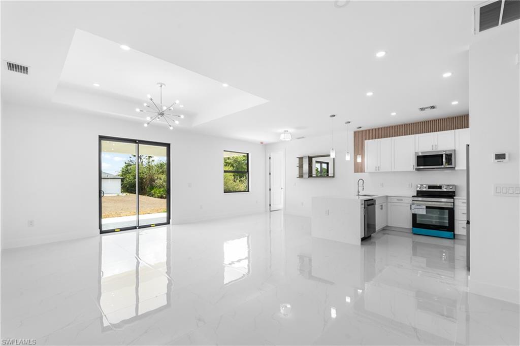 Kitchen with open floor plan, stainless steel appliances, white cabinetry, hanging lights, and light stone counters