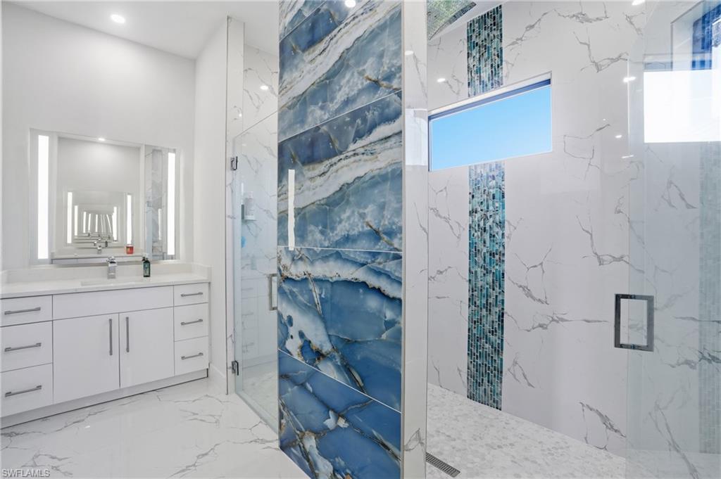 Full bath featuring a marble finish shower, vanity, and light marble finish floors