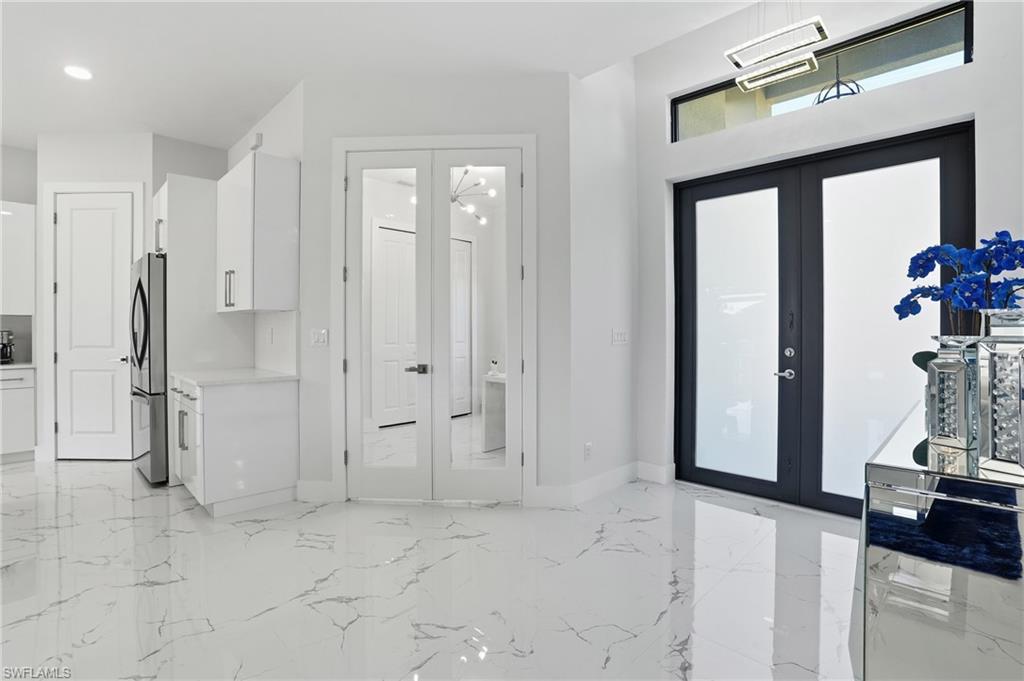 Kitchen featuring french doors, white cabinets, freestanding refrigerator, light marble finish floors, and light stone countertops