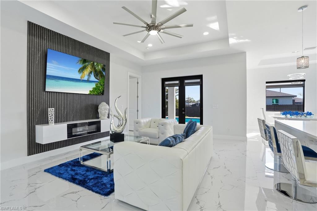 Living area with light marble finish floors, ceiling fan, recessed lighting, french doors, and a tray ceiling
