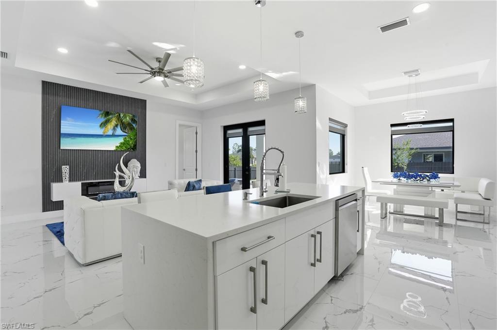 Kitchen with a tray ceiling, white cabinets, an island with sink, open floor plan, and light stone counters