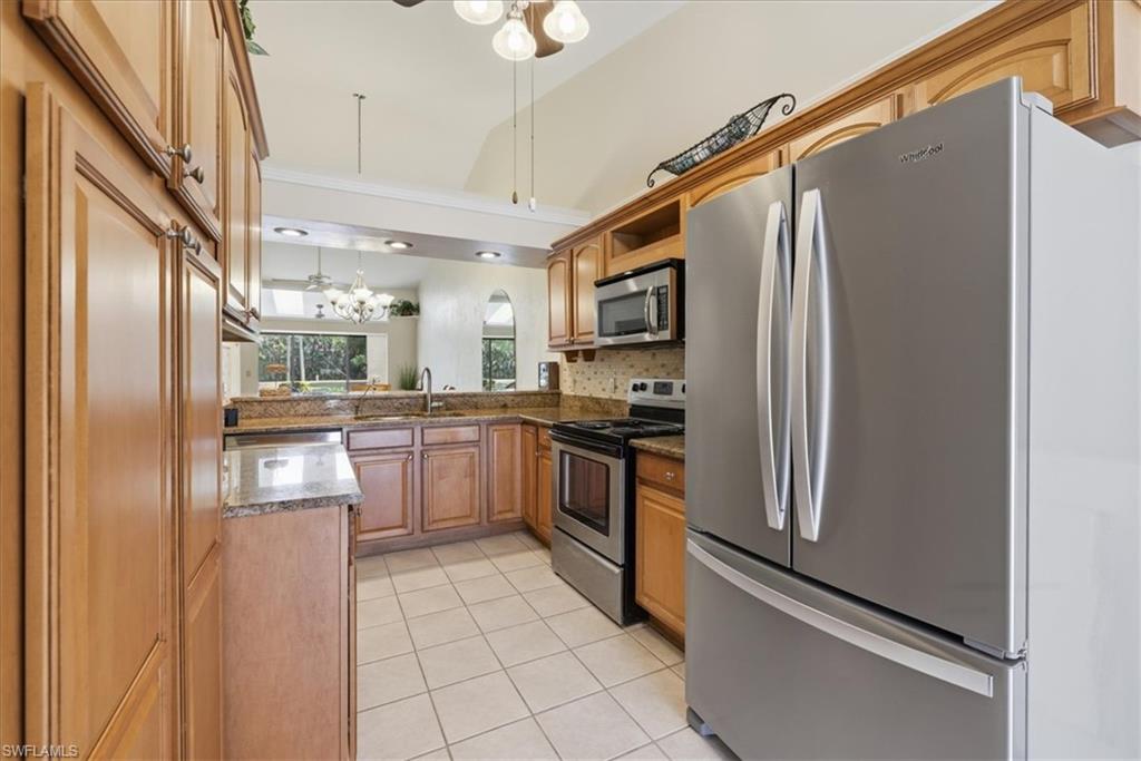 Kitchen featuring stainless steel appliances, dark stone countertops, light tile patterned floors, ceiling fan, and wood finish cabinets
