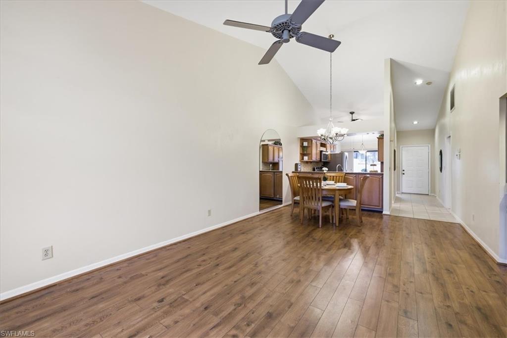 Dining space with dark wood-type flooring, lofted ceiling, ceiling fan, hanging lights, and arched walkways