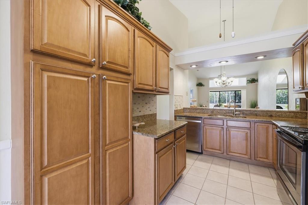 Kitchen featuring dark stone countertops, stainless steel appliances, wood finish cabinetry, tasteful backsplash, and light tile patterned floors