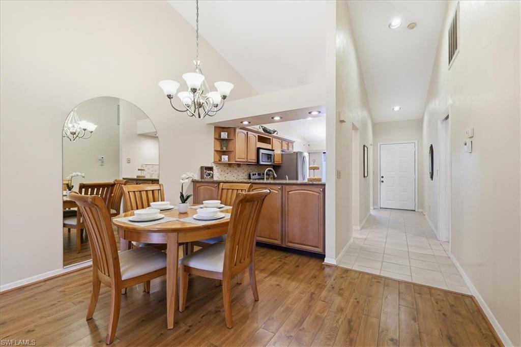 Dining space featuring suspended lighting, light wood-type flooring, arched walkways, and vaulted ceiling