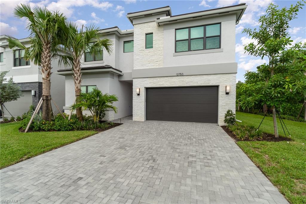 Contemporary home with a front yard, stucco siding, decorative driveway, an attached garage, and stone siding